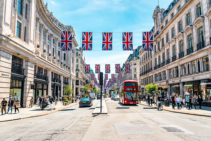 Straße in London mit Fahnen von Großbritannien, einem roten Sightseeing Bus und Leuten