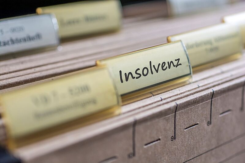 Hängeregister mit gelben Reitern, einer davon beschriftet mit dem Wort „Insolvenz“; die Register sind in einer Schublade oder einem Archivsystem eingeordnet.