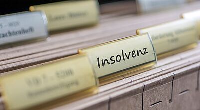 Hängeregister mit gelben Reitern, einer davon beschriftet mit dem Wort „Insolvenz“; die Register sind in einer Schublade oder einem Archivsystem eingeordnet.