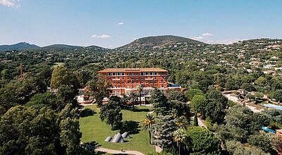 Luxushotel COMO Le Beauvallon an der Côte d’Azur in Frankreich, umgeben von mediterraner Hügellandschaft, Palmen und gepflegtem Gartenpark bei strahlend blauem Himmel.