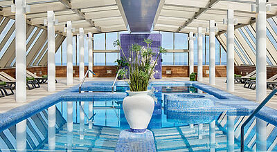 Heller, moderner Spa-Bereich mit überdachtem Innenpool im Hotel Melia Costa Atlantis auf Teneriffa. Der Raum ist von großen Glasfenstern umgeben, die Tageslicht einlassen, und mit weißen Säulen, Liegestühlen und einem zentralen Pflanzgefäß im Pool stilvoll gestaltet