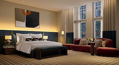 Blick auf ein Bett, rechts unter dem Fenster ist eine Sitzecke