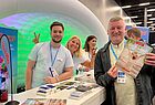Messestand von Alltours mit LED-Beleuchtung, Mitarbeiter am Informationstresen mit Werbebroschüren und Marketingmaterialien bei Messeveranstaltung.