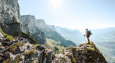 Eine wandernde Frau mit Rucksack steht auf einem Berggipfel