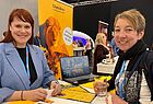 Zwei Frauen am gelben Chamäleon-Stand auf dem jede Menge Werbeartikel liegen 