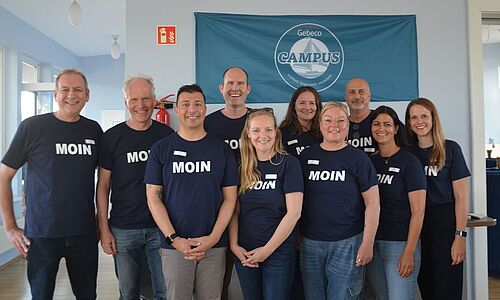 Fünf Frauen und fünf Männer lächeln in die Kamera. Alle tragen ein blaues T-Shirt auf dem Moin steht. 