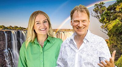Vertriebschefin Katharina Port und Chamäleon-Gründer Ingo Lies führen durch die Live-Streams für Reiseprofis und Kunden. Ein lächelnder Mann und eine lächelnde Frau stehen nebeneinander vor dem Hintergrund eines großen Wasserfalls mit Regenbogen. Die Frau trägt ein grünes Hemd, der Mann ein weißes Hemd mit geometrischem Muster. Der Himmel ist blau und die Szene wirkt hell und freundlich.
