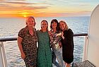 Vier Frauen in Abendgarderobe auf einem Balkon. Im Meer geht die Sonne unter