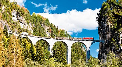 Ein Zug fährt über ein Steinviadukt mit mehreren Bögen, das sich über eine tiefe Schlucht spannt
