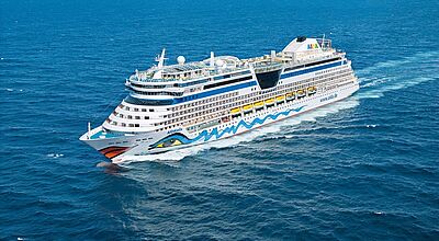 Ein Aida-Kreuzfahrtschiff mit dem markentypischen Kussmund und dem bunten Auge am Bug in Fahrt auf blauem Meer