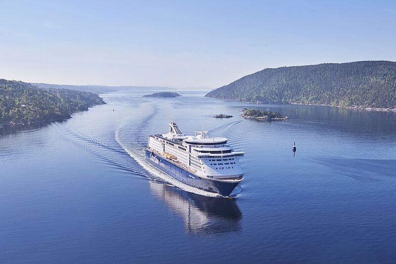 Eine große Kreuzfahrtfähre fährt durch die norwegischen Fjorde. Das Wetter ist gut.
