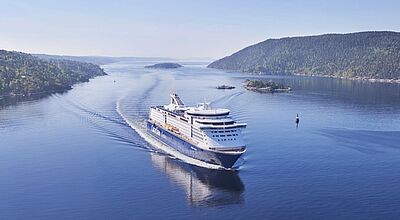 Eine große Kreuzfahrtfähre fährt durch die norwegischen Fjorde. Das Wetter ist gut.