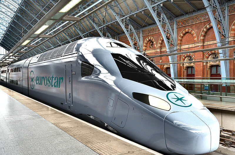 Ein moderner Eurostar Hochgeschwindigkeitszug steht am Bahnsteig eines historischen Bahnhofs in Europa. Das silberne Zugdesign und die auffällige Eurostar-Beschriftung sind deutlich zu erkennen. Im Hintergrund ist die imposante Architektur des Bahnhofs mit Ziegelwänden und Stahlträgern zu sehen.