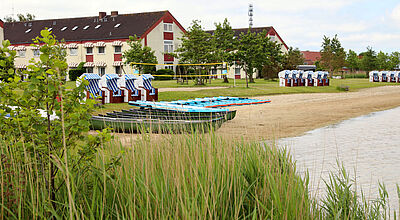 Einfaches Strandhotel, davor Strandkörbe, Wasser und Grün