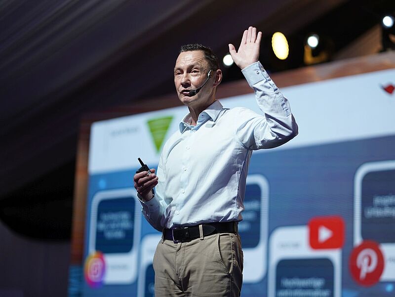 Bei einer Tagung steht ein Redner mit Headset auf der Bühne und richtet sich ans Publikum.