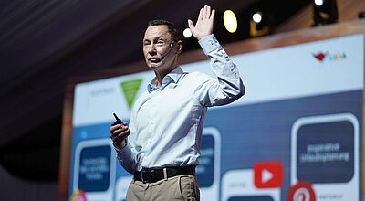 Bei einer Tagung steht ein Redner mit Headset auf der Bühne und richtet sich ans Publikum.