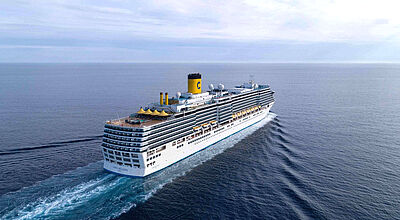 Die Costa Deliziosa nimmt bei ihrer 139-tägigen Weltreise Kurs auf 29 Länder. Foto: Costa Kreuzfahrten Luftaufnahme eines Kreuzfahrtschiffs mit gelbem Schornstein, das über ein dunkelblaues Meer fährt