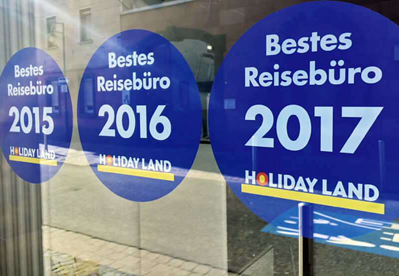 Plakative Eigenwerbung von Holiday Land: Die Kette vergibt seit Jahren den Titel „Bestes Reisebüro“ Plakative Eigenwerbung von Holiday Land: Die Kette vergibt seit Jahren den Titel „Bestes Reisebüro“