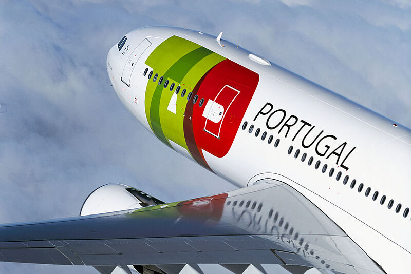Nahaufnahme eines Flugzeugrumpfs und einer Tragfläche der Airline TAP Air Portugal von schräg oben während eines Fluges über Wolken.