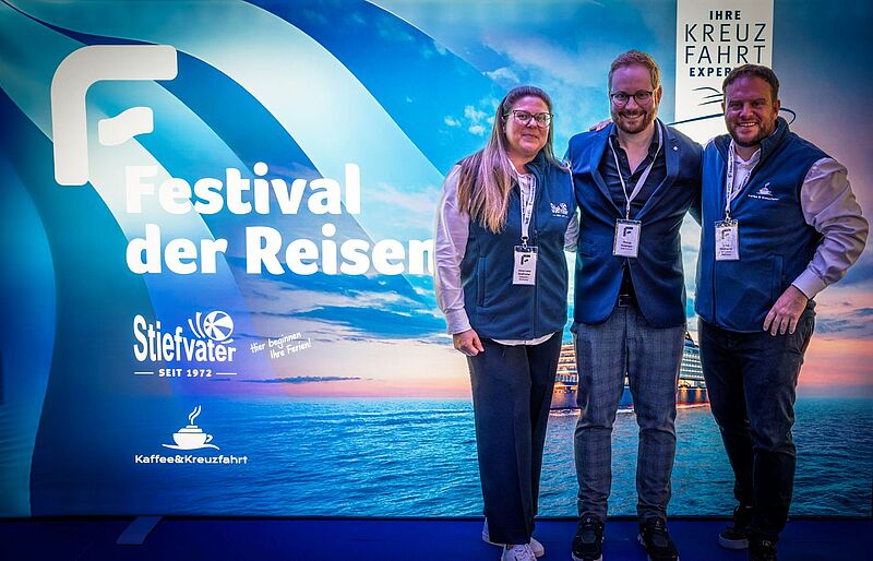 Glücklich über ein erfolgreiches Event (von links): Die Reisebüro-Inhaber Anna Lena (links) und Aron Stiefvater mit Philipp Holzinger als Vertreter des Top-Sponsors MSC Cruises. Drei Personen stehen lächelnd vor einem blau beleuchteten Messe- oder Event-Hintergrund mit der Aufschrift Festival der Reisen. Sie tragen Namensschilder und dunkelblaue Westen. Hinter ihnen ist ein Meer- und Kreuzfahrtmotiv zu sehen