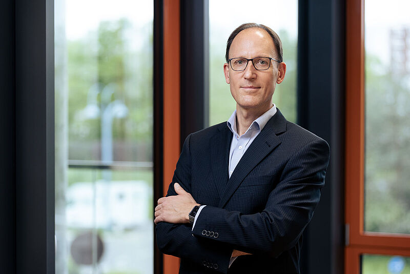 LTA-Chef Michael Dorka setzt nun auf die ERV als neuen Risikoträger Ein Mann im Business-Anzug steht mit verschränkten Armen vor einem großen Fenster in einem modernen Bürogebäude; das Bild vermittelt Professionalität und Führungskompetenz im Unternehmensumfeld.