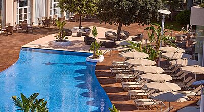 Am Rand eines Pools stehen viele Liegen mit Sonnenschirmen