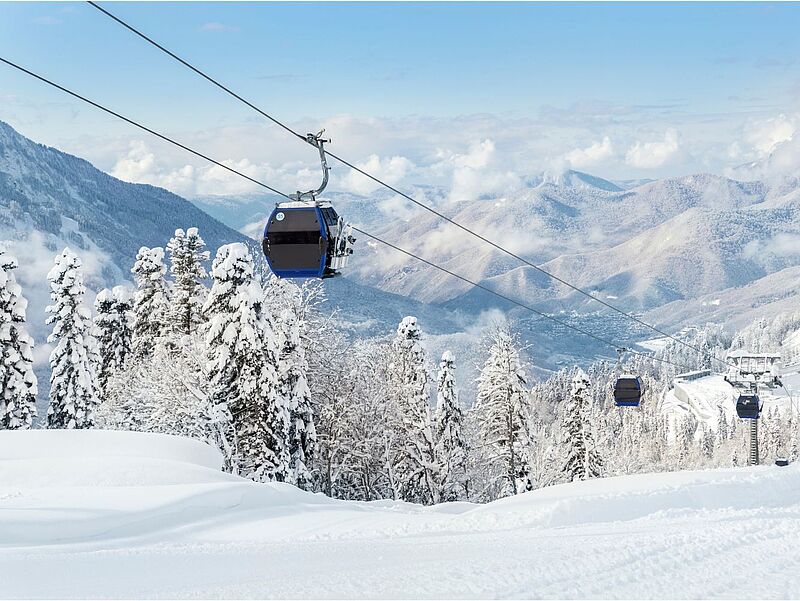 Bild von einer Berglandschaft mit Schnee unter blauem Himmel und einem modernen Skilift.