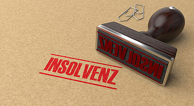 Das Wort Insolvenz wurde auf einen Briefumschlag gestempelt. Der Stempel sowie zwei Büroklammern liegen daneben.