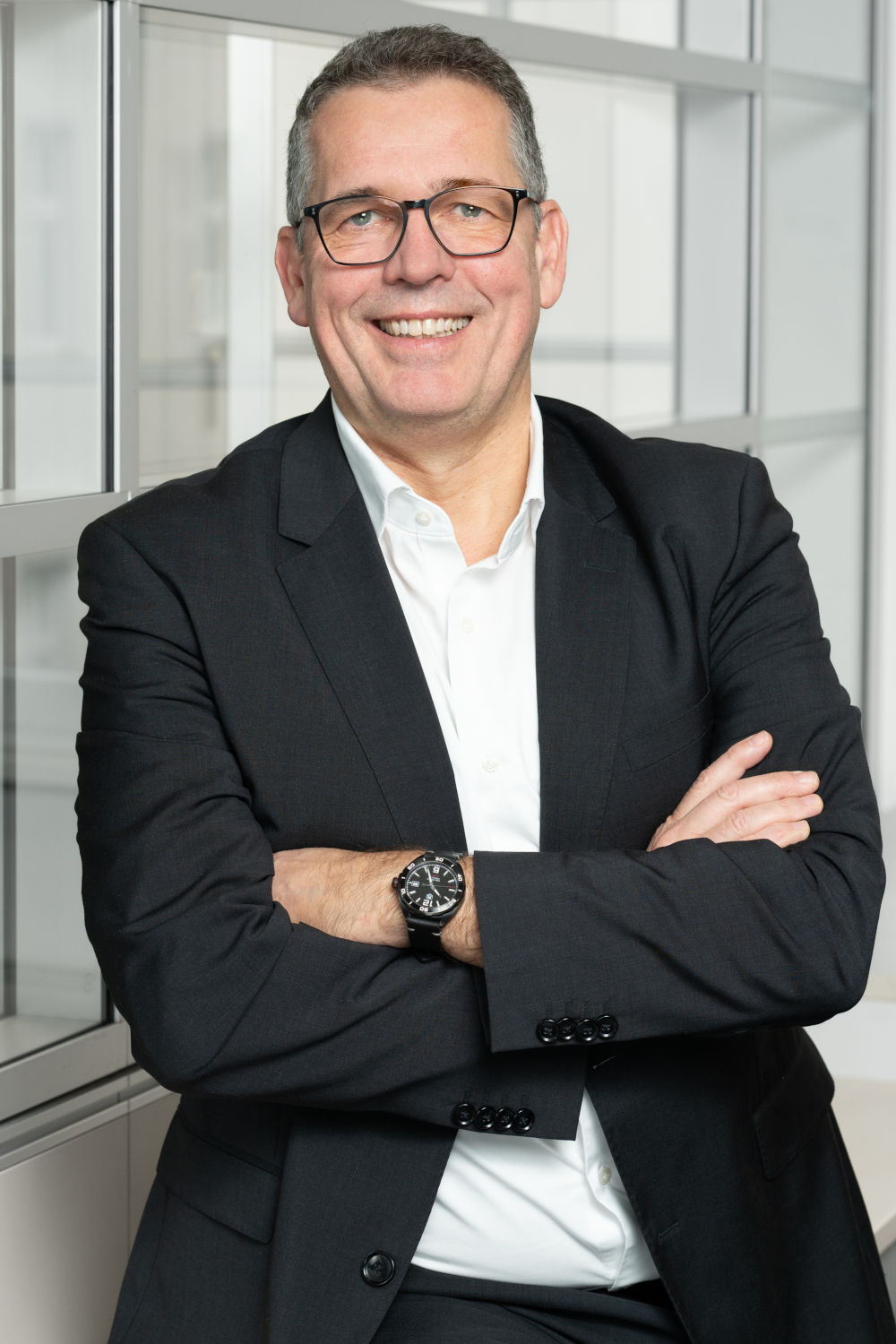 Ex-Amadeus-Manager Holger Taubmann steht seit Juli an der Spitze der Aerticket-Gruppe. Ein Manager mittleren Alters in schwarzem Jackett und weißem Hemd steht mit verschränkten Armen vor Fenstern eines Bürogebäudes