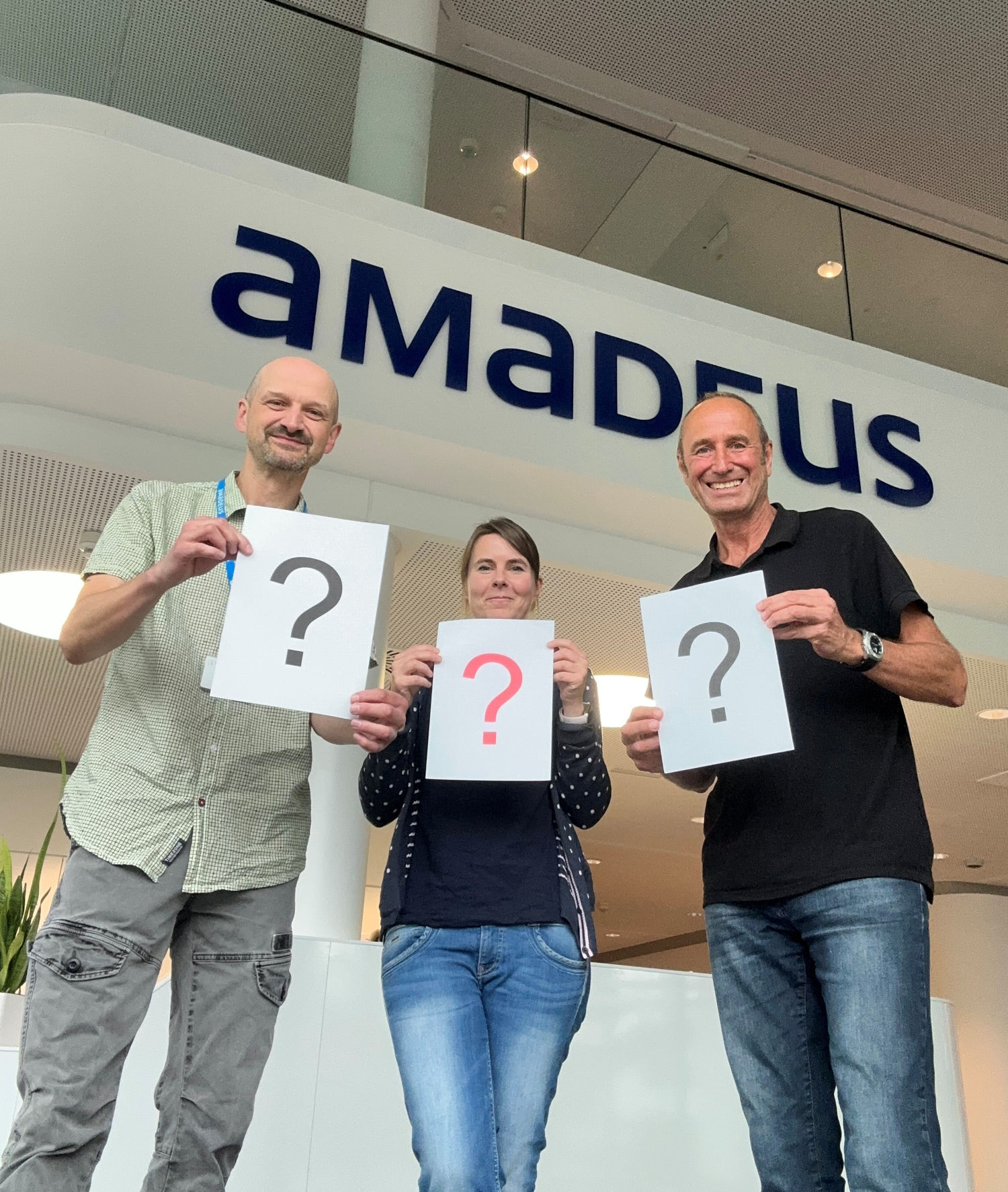 Kamen mit vielen Fragen nach Bad Homburg: ta-Redakteure Thomas Riebesehl, Ute Fiedler und Matthias Gürtler. Foto: ta Drei Personen stehen vor einem Schild mit der Aufschrift ‚Amadeus‘ und halten jeweils ein Blatt Papier mit einem großen Fragezeichen in den Händen. Die mittlere Person hält ein rotes Fragezeichen, die beiden äußeren schwarze.