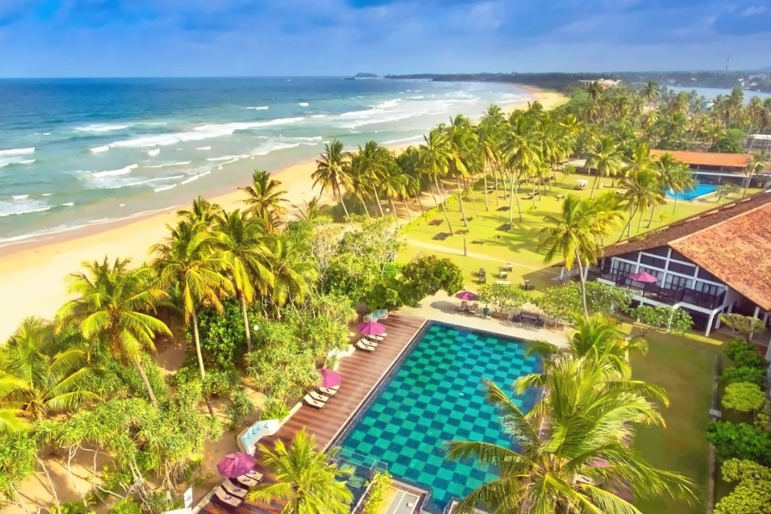 Das Dickwella Resort & Spa auf Sri Lanka ist eines von 44 neuen Hotels im Programm von Anex, Bucher und Neckermann Luftaufnahme eines tropischen Strandresorts mit großem Pool, Palmen und weißem Sandstrand am türkisblauen Meer.