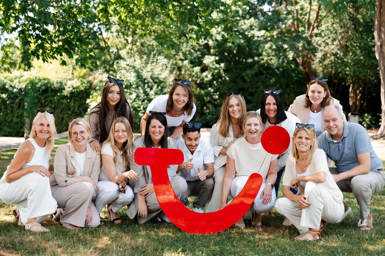 Das Team der TUI-Filiale in Aschaffenburg 15 Leute lächeln in die Kamera. Sie posieren im Freien hinter einem großen roten TUI-Logo