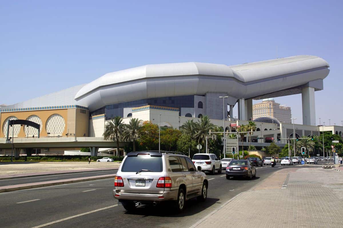 Eine mehrspurige Straße in Dubai führt an einem großen Gebäude mit einer markanten, röhrenförmigen Skihalle vorbei, während Autos den Bereich befahren.