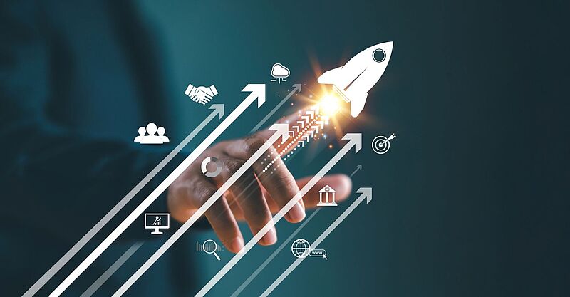 Im Vordergrund ist eine Hand zu sehen, die eine aufsteigende Rakete und Pfeile mit Geschäftssymbolen wie Zielscheibe, Netzwerk und Wachstum auslöst. Das Bild steht für Fortschritt, Start-up-Erfolg und Online-Business-Strategien. 