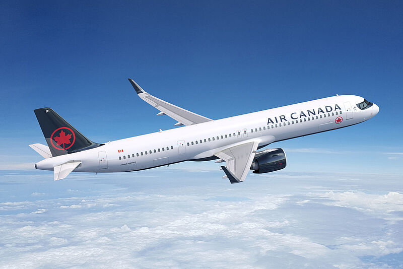 Ein Flugzeug von Air Canada in weiß-schwarzer Lackierung und rotem Ahornblatt-Logo auf der Heckflosse fliegt vor blauem Himmel über einer Wolkendecke.