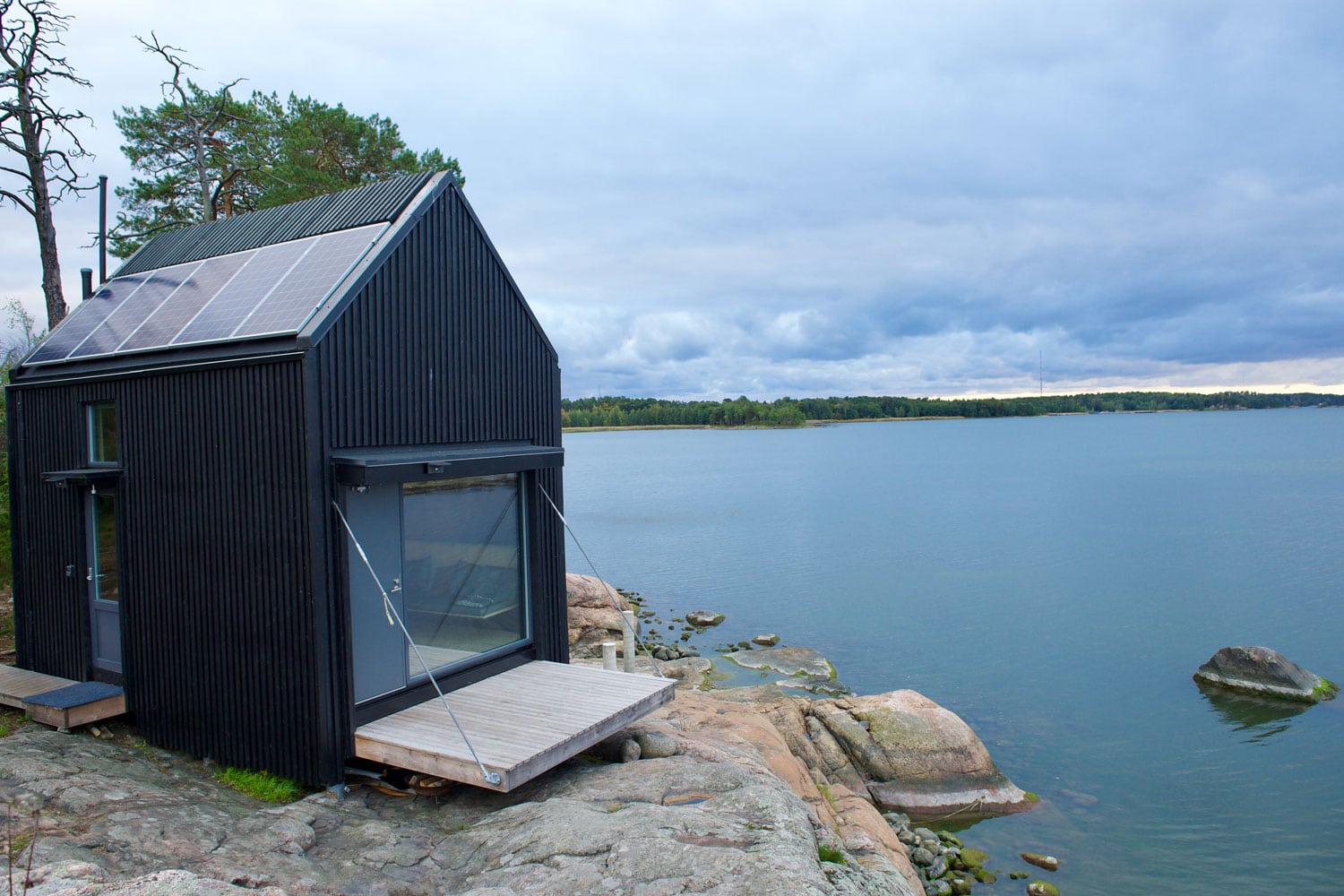 Kleines, schwarzes Holzhaus mit Terrasse auf einem Felsen am Meer