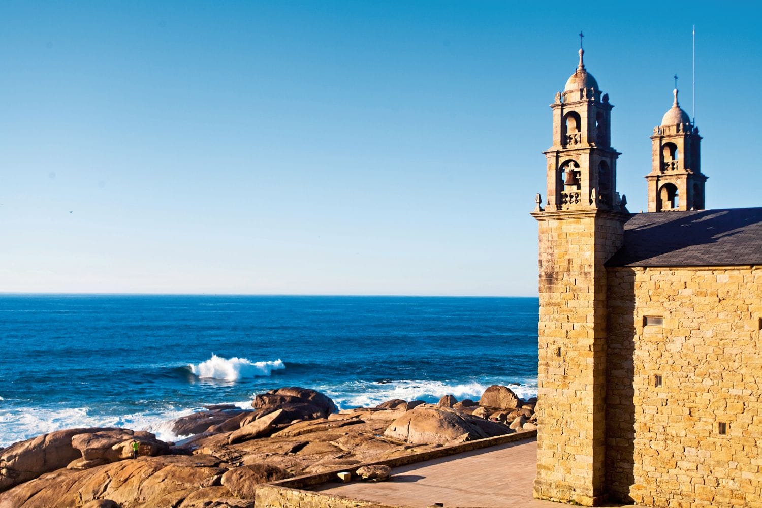 Rechts sieht man die Kirchstürme einer Kirche, links viele Steine und das Meer