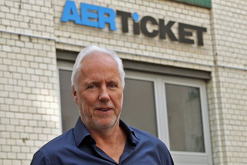 Rainer Klee, der Geschäftsführer des Flugticket-Großhändlers Aerticket, steht vor dem weißen Firmengebäude mit Aerticket-Logo. Der ältere Mann mit grauen Haaren ist bekleidet mit einem blauen Hemd.