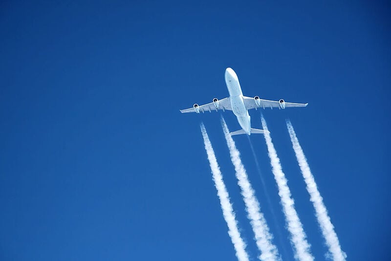 Ansicht auf die Unterseite eines fliegenden Flugzeugs mit Kondensstreifen vor blauem Himmel