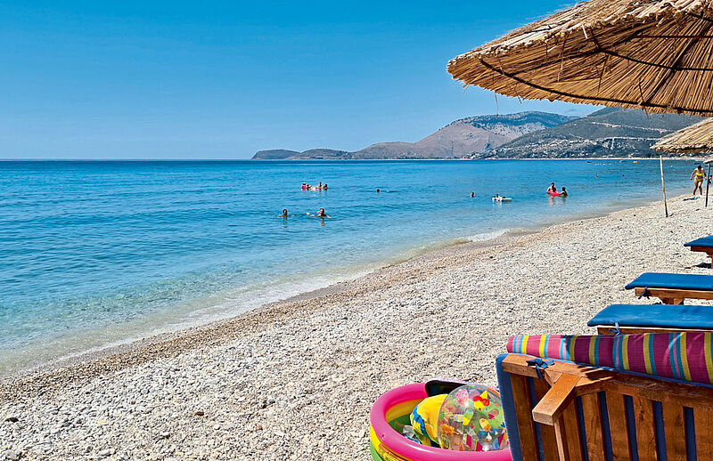 Ein Strand mit Sonnenschirmen und Liegestühlen mit Blick auf das Meer mit Badegästen