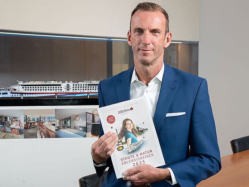 Arosa-Vertriebschef Stefan Sprunk mit Katalog 2025 vor Schiffsmodelloto: Arosa