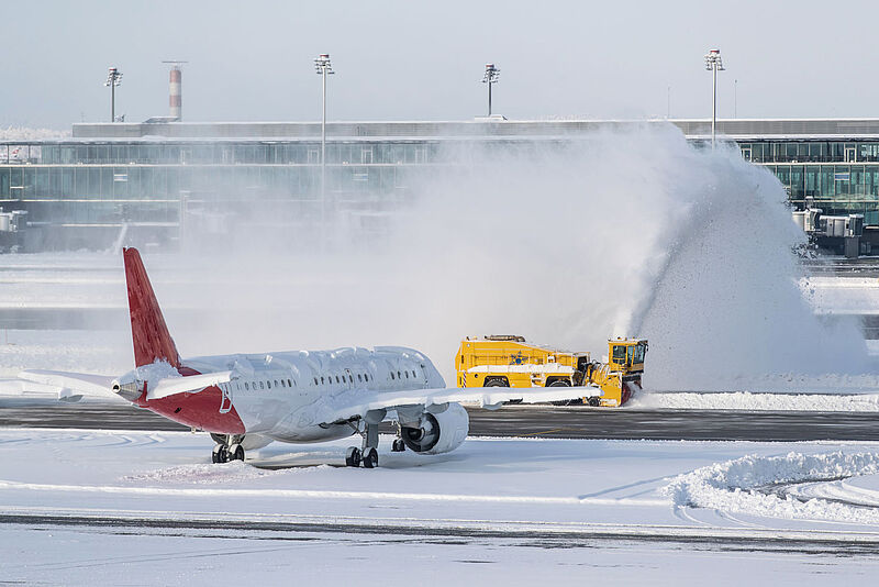 Flughafen mit schneebedecktem Vorfeld und Schneeräumfahrzeug