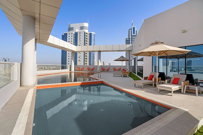 Rooftop-Pool im Hotel Barcelo in Manama, Bahrain mit Sonnenliegen, modernen Sitzbereichen und Blick auf die Skyline – luxuriöse Dachterrasse mit Stadtblick für erholsamen Aufenthalt im Nahen Osten.