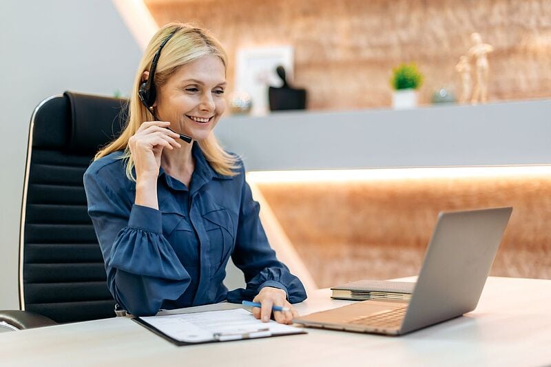 Lächelnde Frau mit Headset sitzt in einem Büro vor Laptop