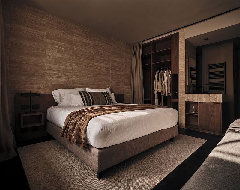 Blick in ein recht dunkles Zimmer mit erdigen Tönen, im Hintergrund ein offener Kleiderschrank