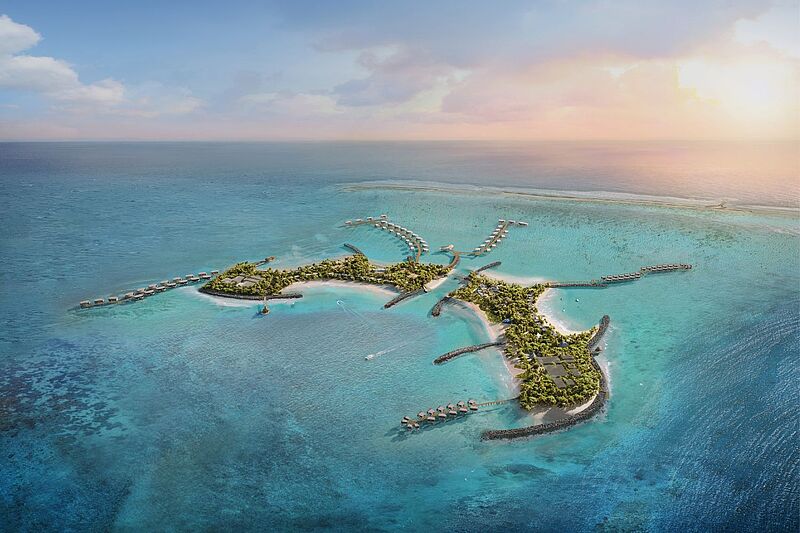 Ein Luftbild eines luxuriösen Multi-Insel-Resorts inmitten eines türkisfarbenen Ozeans. Die Inseln sind durch Holzstege verbunden, die zu Überwasser-Bungalows führen. Das Resort ist von weißen Sandstränden, üppigem Grün und Korallenriffen umgeben. Boote sind im klaren Wasser sichtbar, während die Sonne den Horizont in warme Farbtöne taucht.