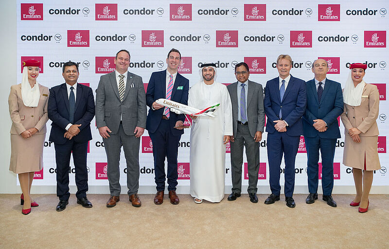 Gruppenaufnahme von Managern und Crewmitglieder von Emirates und Condor bei der Ankündigung ihrer Codeshare-Partnerschaft mit Logos im Hintergrund. Zwei Manager halten ein Flugzeugmodell von Emirates.