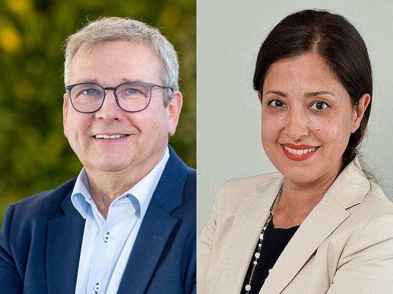 Zwei Personen im Porträt nebeneinander. Links ein älterer Mann mit grauen Haaren, Brille, hellem Hemd und dunkelblauem Sakko, er lächelt in die Kamera. Rechts eine Frau mit dunklen Haaren, die nach hinten gebunden sind, hellem Blazer, dunklem Oberteil und Kette, ebenfalls lächelnd.