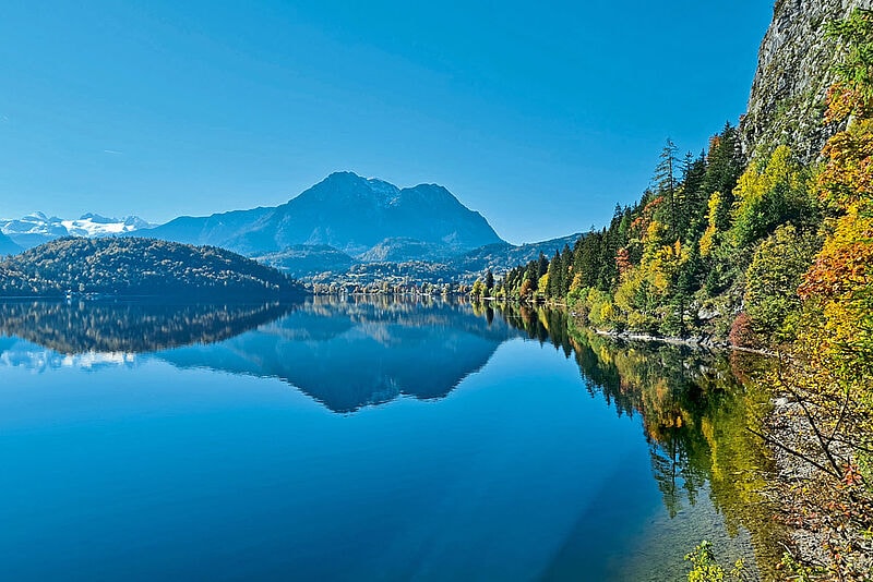 Blaue Wasseroberfläche auf dem Altausseer See gesäumt von waldigem Ufer, Berge in der Ferne 