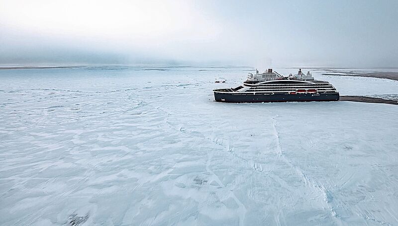 Das Expeditionskreuzfahrtschiff Le Commandant Charcot liegt im arktischen Eis, umgeben von einer endlosen weißen Schneelandschaft